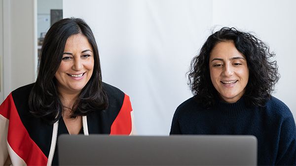 Zwei Frauen ebenfalls vor einem Mac Book in einem Online-Meeting
